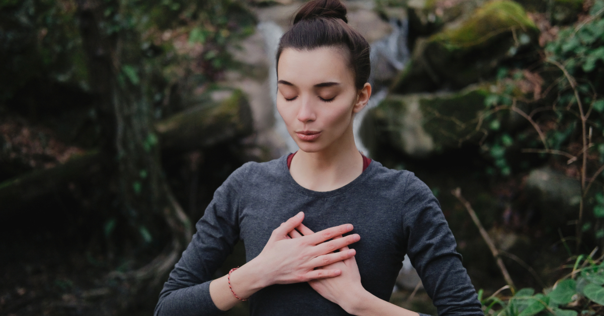 woman sitting with her hands over her heart practicing breathing exercises